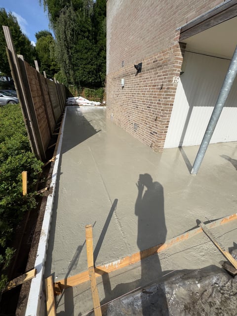 Wet concrete path alongside brick building with wooden fence and green hedges