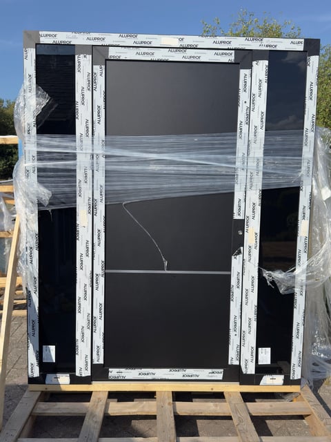 Double-pane window frame with white aluminum mullions and black vinyl components on wooden pallet during installation