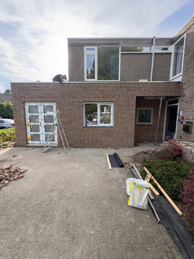 Modern brick residential home under construction with ladder, tools, and materials scattered in front yard on a cloudy day